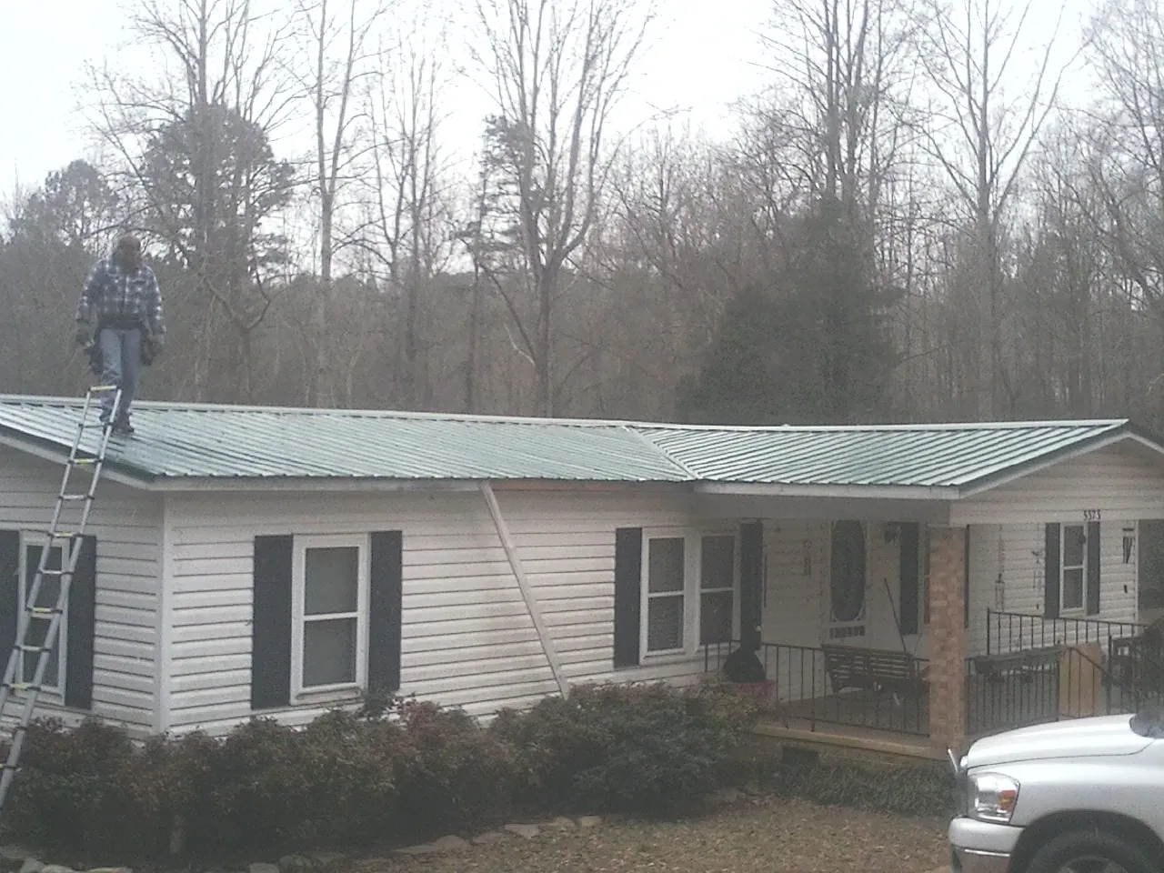 Worker on a ladder beside a new green metal roof on a ranch home in Fort Jennings