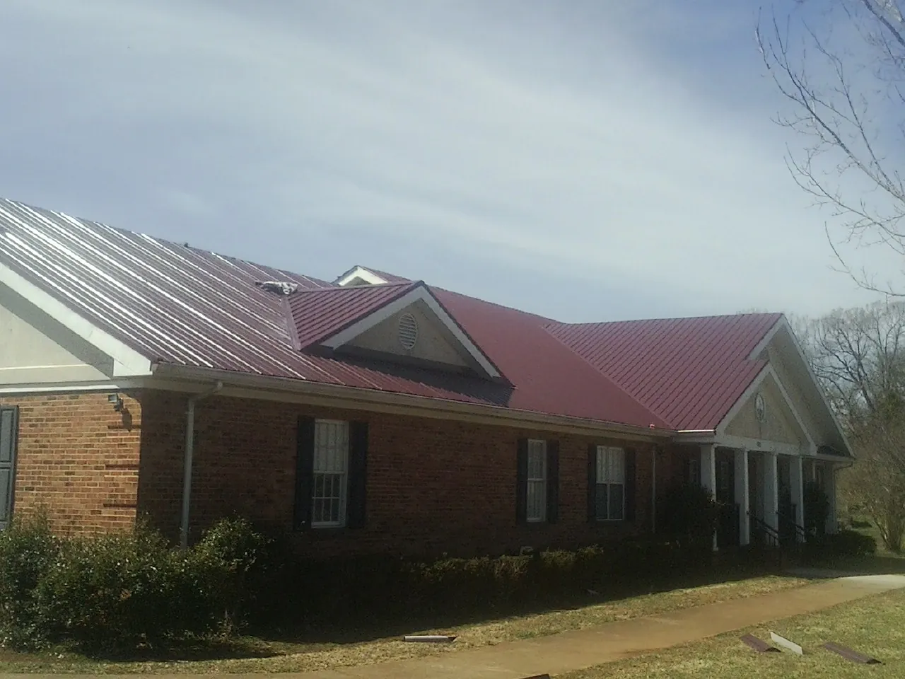 Red metal roof with gabled entries on a long brick building, from a Hail Damage Roof Repair job in Fort Jennings