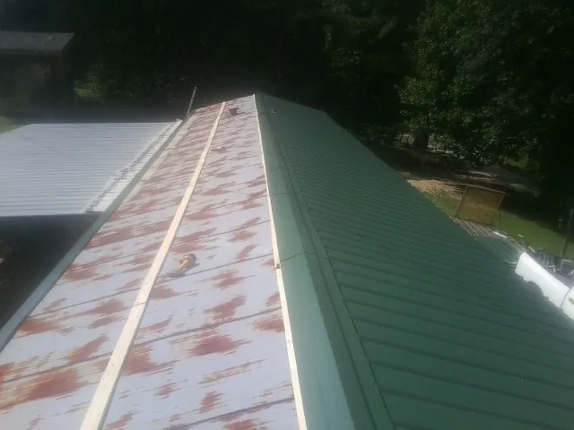 Old rusted panels beside newly installed green metal roofing — Wind Damage Roof Repair by Roofing Brothers in Fort Jennings