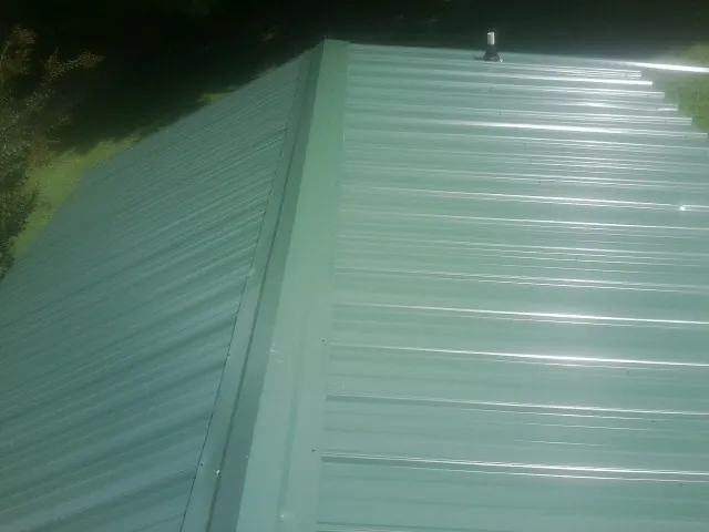 New green metal panels meeting at the ridge of a roof — Flat Roof Repair work by our crew in Fort Jennings