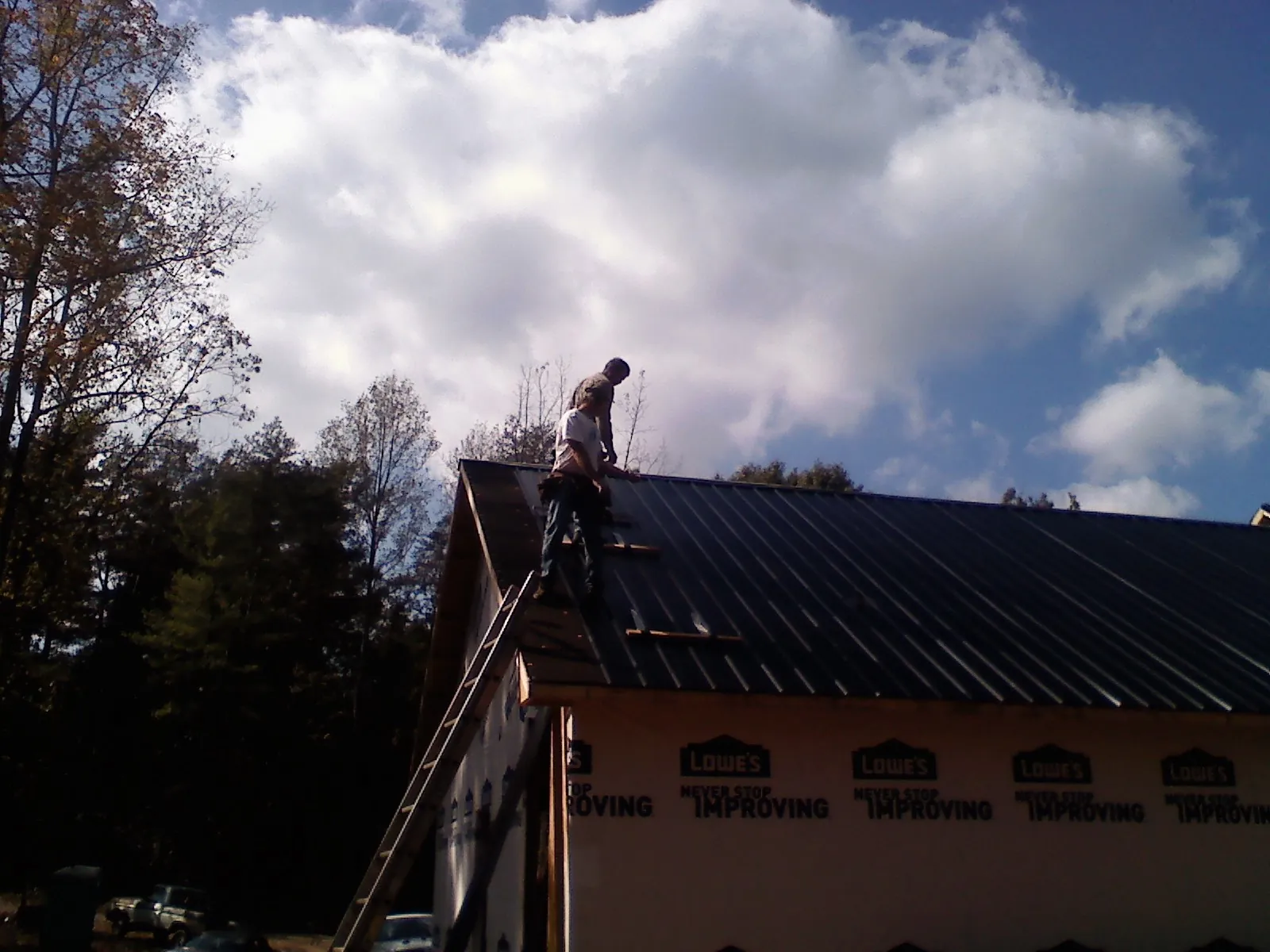 Roofer fastening dark metal panels high against a cloudy sky, from a Roof Inspection job in Fort Jennings