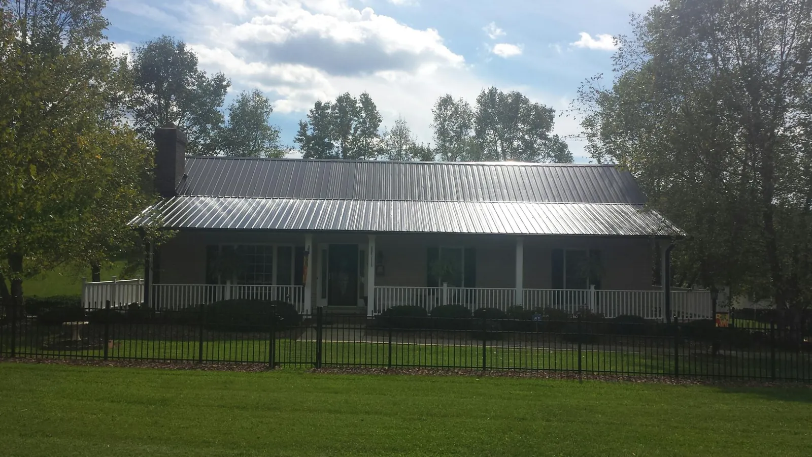 Gray metal roof on a brick ranch with a full width front porch — Gutter Guard Installation work by our crew in Fort Jennings
