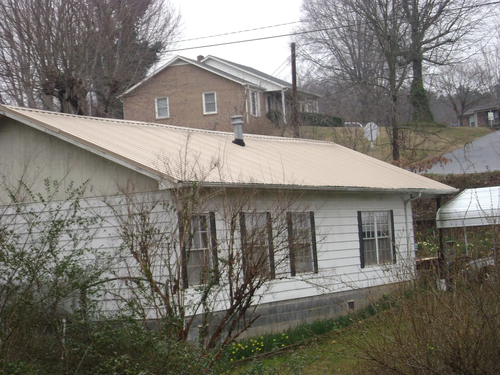 Tan metal roof on a white sided house set into a hillside — Commercial Roofing by Roofing Brothers in Fort Jennings